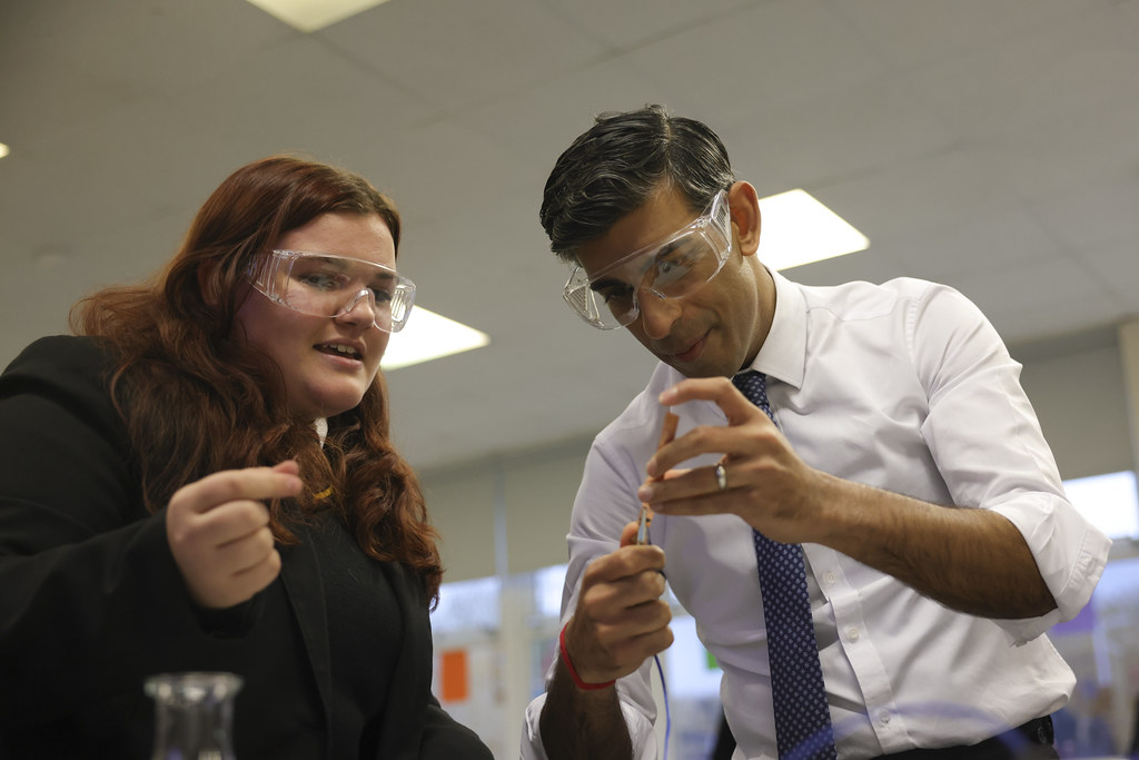Two people wearing science googles complete an experiment using a glass beaker and a tube